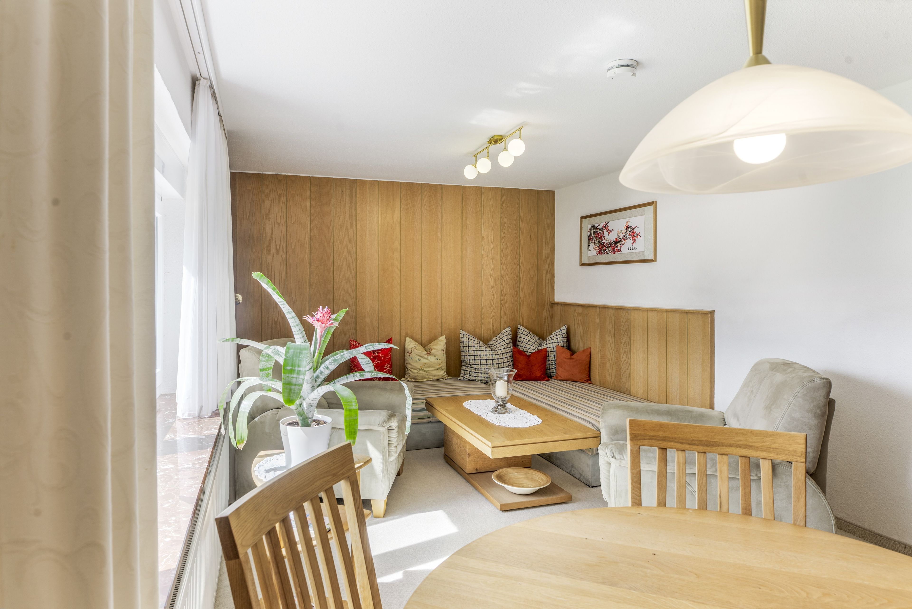 Un salon moderne avec un mur lambrissé en bois, un canapé agrémenté de coussins à motifs, une table à manger avec des chaises et un luminaire suspendu.
