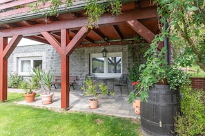 Un patio techado con pared de piedra, vigas de madera y plantas en macetas.