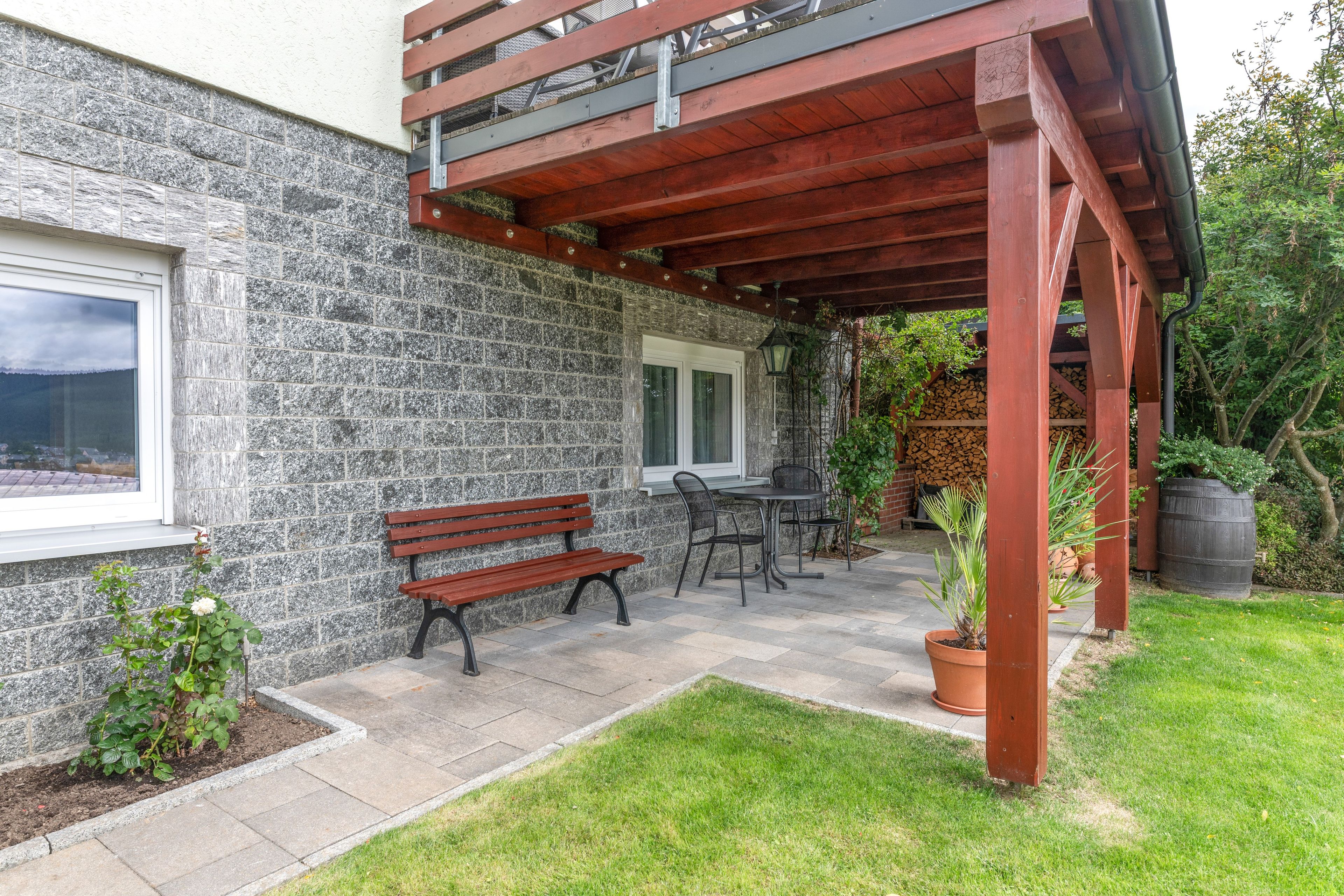 Eine Terrasse mit einer Steinmauer, einer Holzbank, einem Tisch mit Stühlen und einer Pergola.