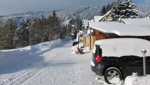 Une route enneigée, avec une voiture garée et un bâtiment doté d’un toit en pente.