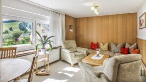 Un salon avec vue sur un paysage verdoyant, un mur en bois, un ensemble de canapés et une table à manger.