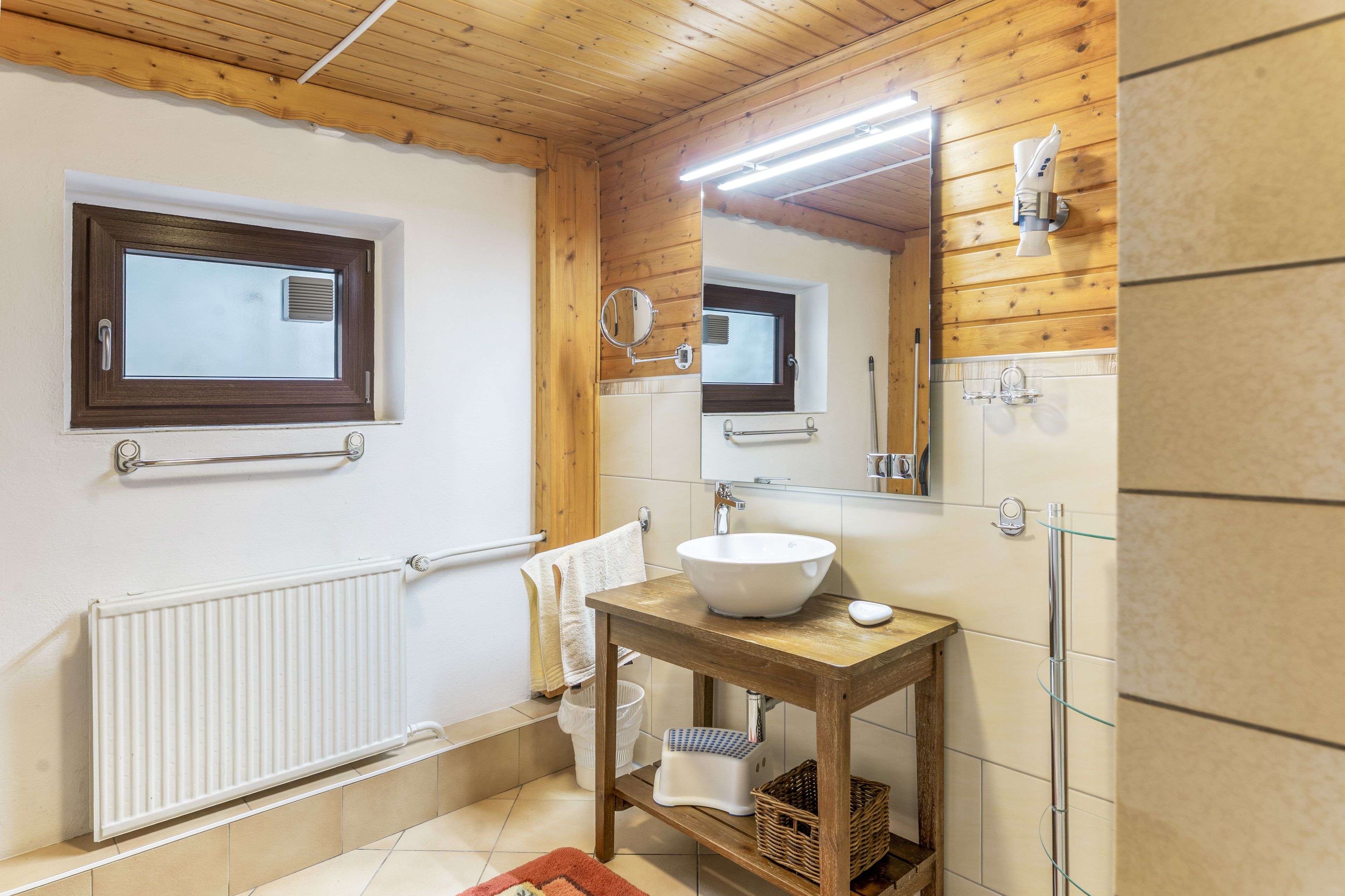 Ein Badezimmer mit Holzboden, einem weißen Waschbecken, einem Spiegel und einem Handtuchhalter.
