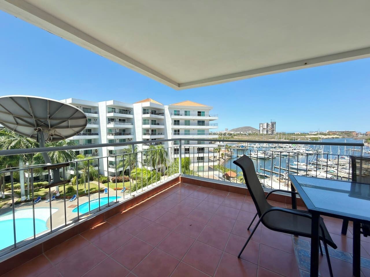A balcony with a view of a swimming pool, a dining table, and chairs.