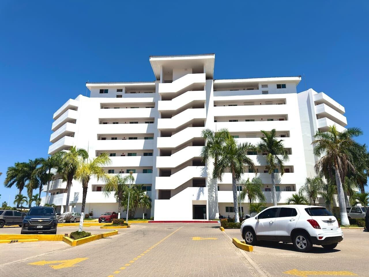 A multi-story hotel with a central atrium, parking lot, and palm trees.