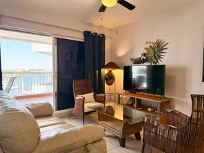 A living room with a sofa, armchairs, a coffee table, a TV, and a balcony with a view. - Elegante Departamento en Costa Veleros (Mazatlán)