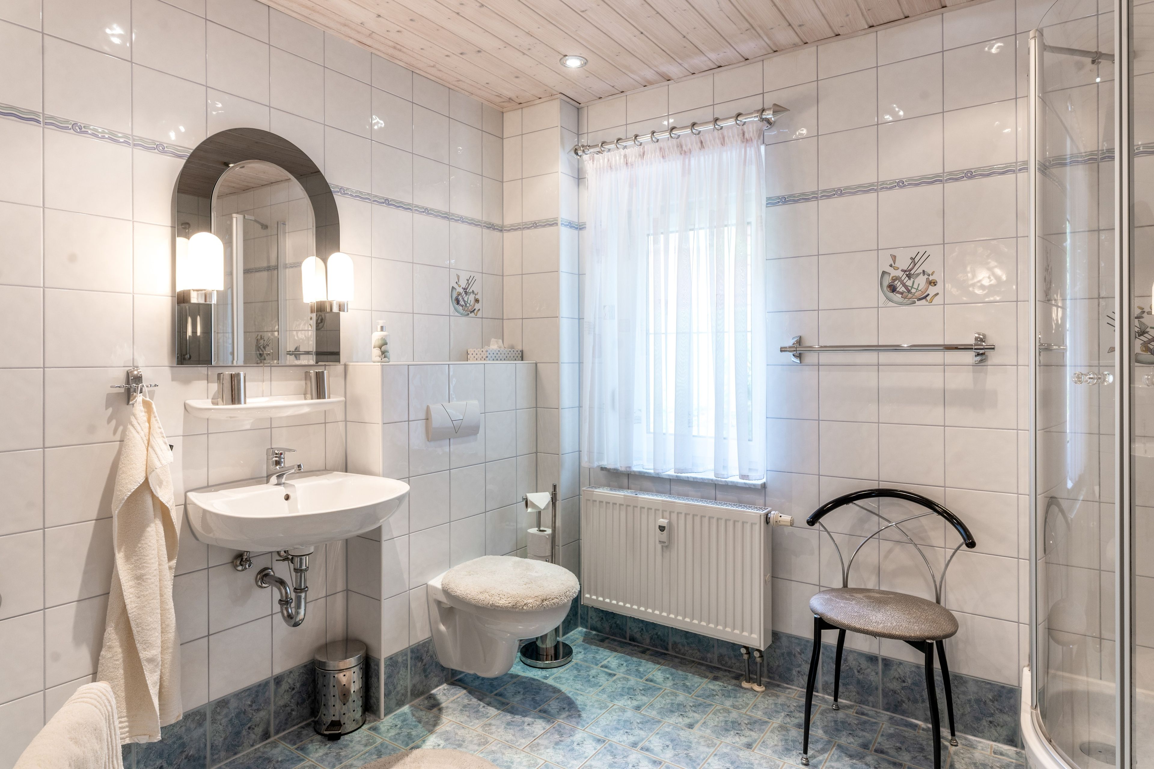 Ein Badezimmer mit Waschbecken, Spiegel, Toilette, Dusche und einem Fenster mit Vorhängen.