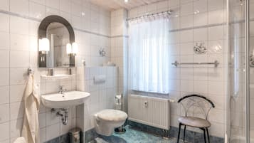 Ein Badezimmer mit Waschbecken, Spiegel, Toilette, Dusche und einem Fenster mit Vorhängen.