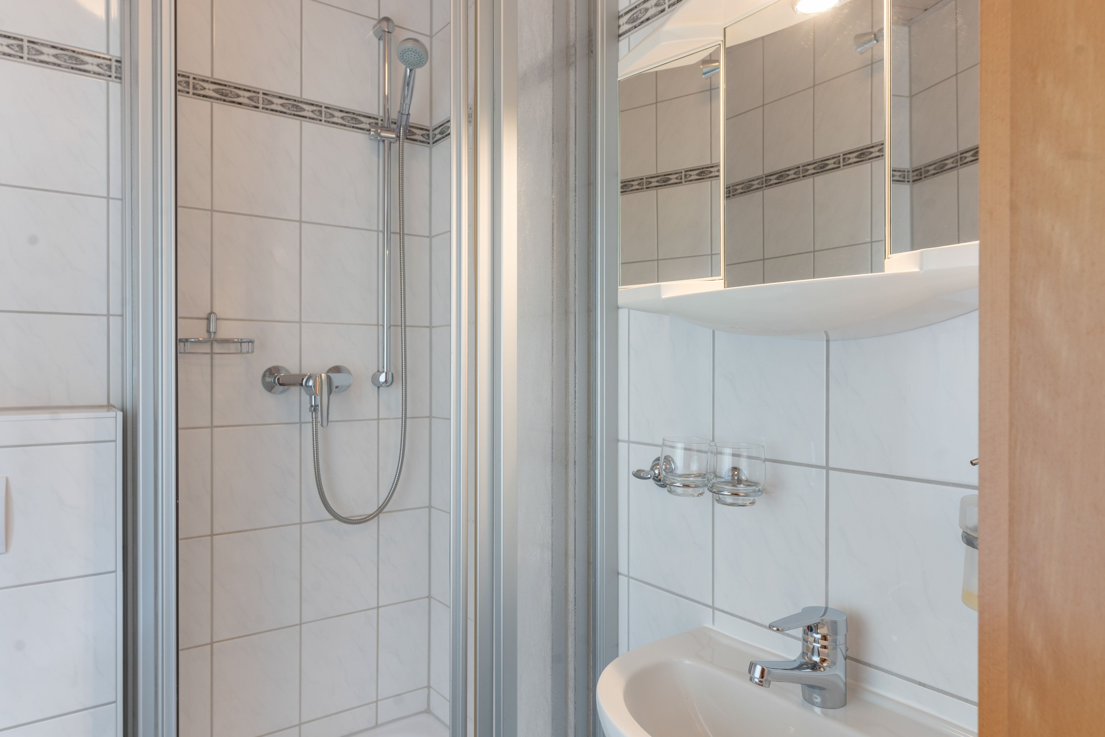 Une salle de bain avec une douche à parois de verre, un lavabo avec un miroir au-dessus et un mur recouvert de carreaux.