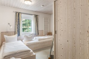 Un dormitorio con dos camas, una ventana con cortinas, una lámpara de noche y un armario de madera.