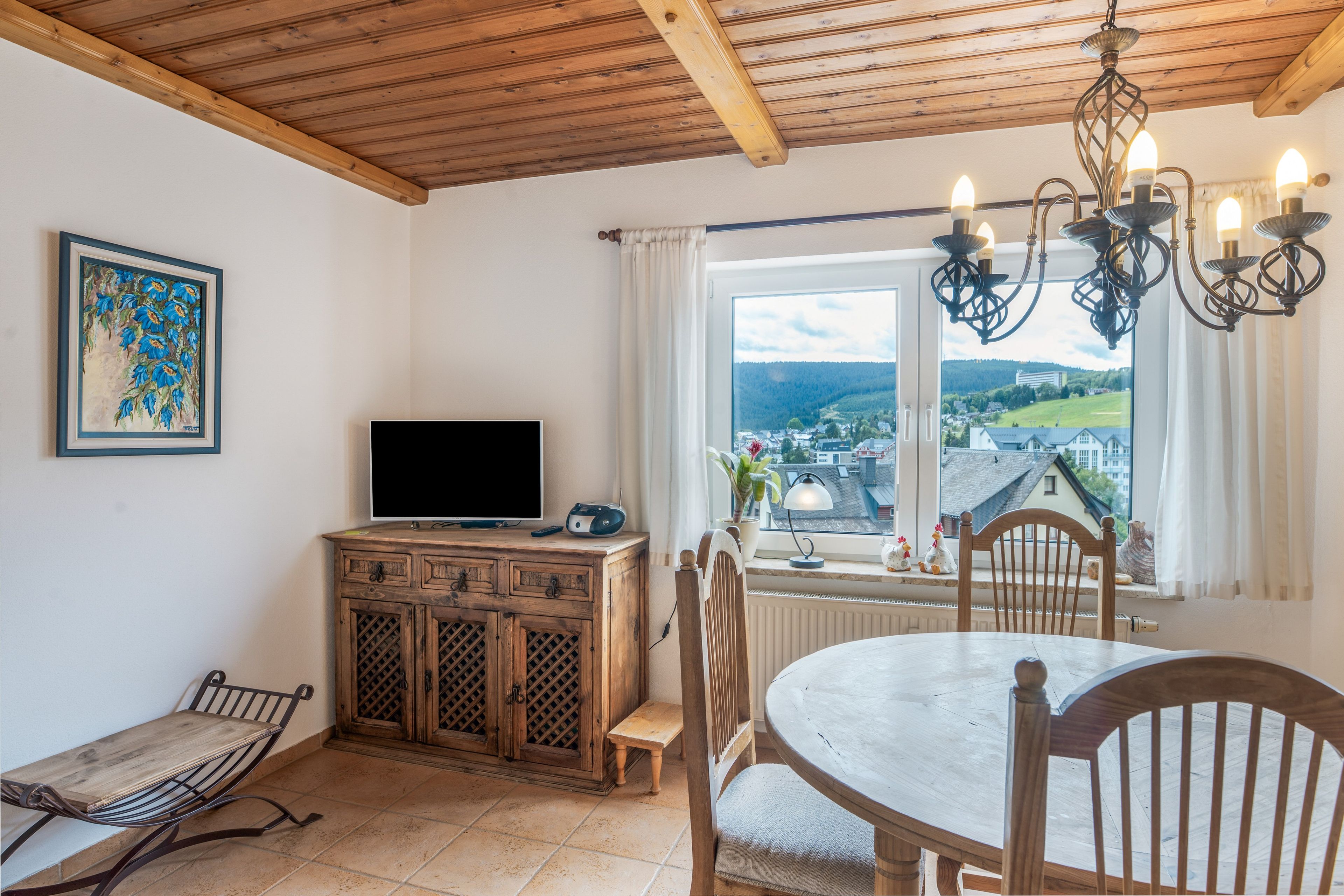 Une pièce avec un plafond en bois, un téléviseur posé sur un meuble, une table à manger avec des chaises et une fenêtre donnant sur la ville.