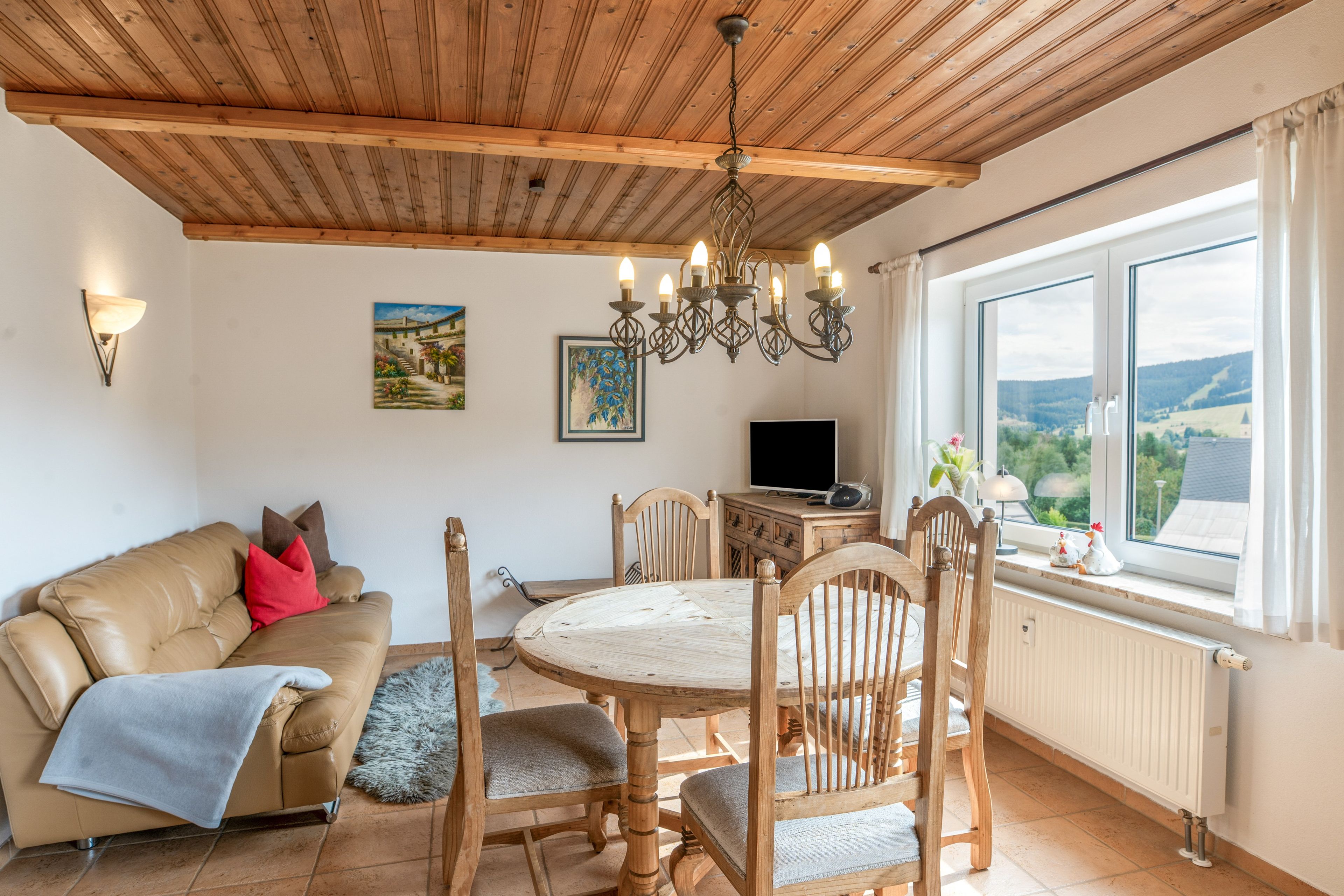 Uma sala de estar aconchegante com teto de madeira, uma mesa de jantar com cadeiras, um sofá com almofadas, uma televisão e uma janela com vista.