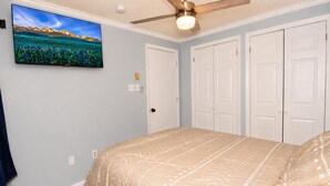 Une chambre à coucher comprenant un lit, un ventilateur de plafond, un téléviseur fixé au mur et un ensemble de portes blanches.