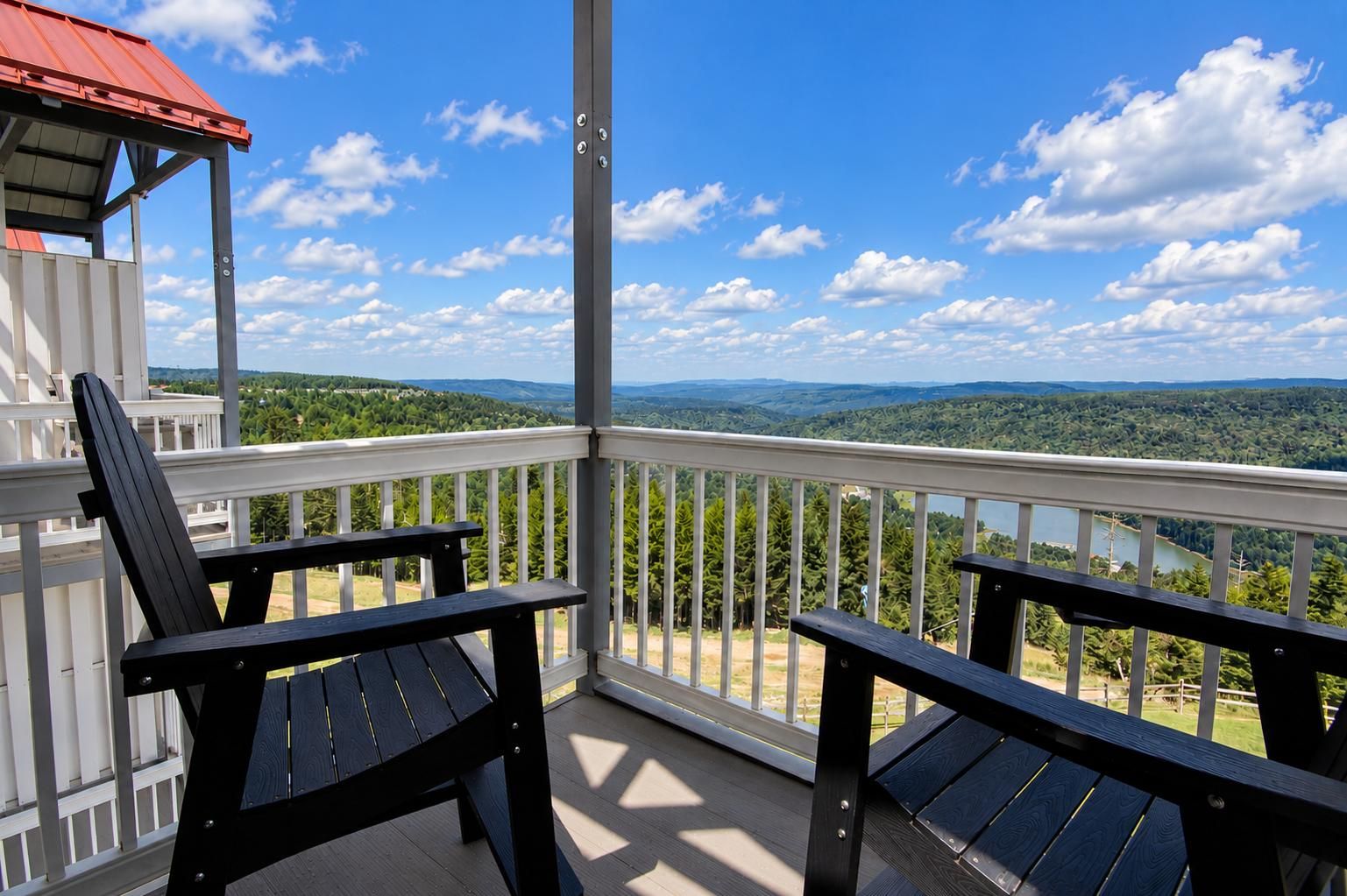 A balcony with two Adirondack chairs, a white railing, and a scenic view of a lake and mountains.