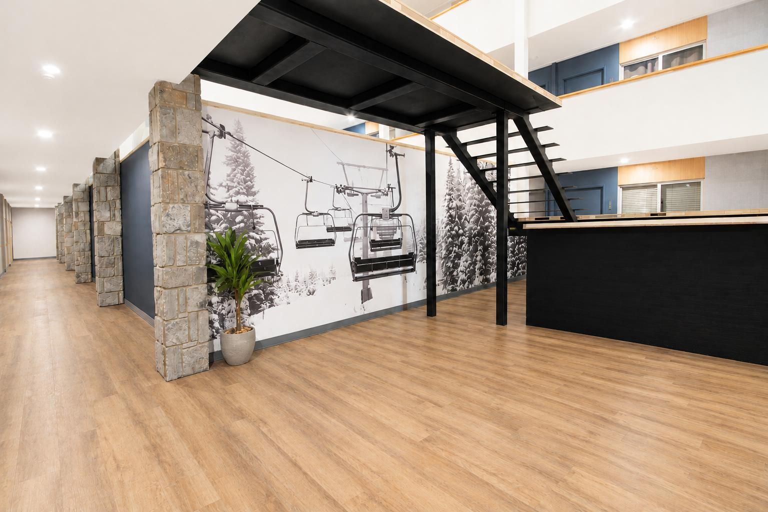 A modern interior with a reception desk, stone pillars, a ski lift mural, and a staircase.