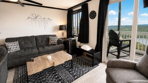 Un salon moderne avec un canapé, une table basse, une cheminée, une horloge et une vue sur l’extérieur.