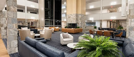 A spacious lobby with a high ceiling, stone pillars, leather seating, and a central plant.
