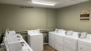 Une buanderie équipée de plusieurs lave-linge et sèche-linge Whirlpool, un panneau indiquant qu’il est interdit de mettre des bottes ou des chaussures dans les machines à laver ou les sèche-linge, et un avertissement concernant le risque que les sèche-linge endommagent les vêtements de ski.