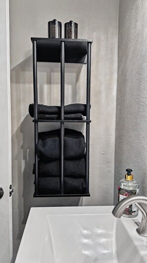 Ein Badezimmer mit einem schwarzen Handtuchhalter, gefalteten Handtüchern, einer Seifenspenderflasche und einem weißen Waschbecken.