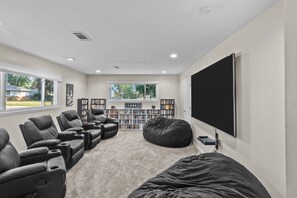 A home theater room with a large flat-screen TV, multiple recliner chairs, a bean bag, and two bookshelves filled with books. - My Happy Place! "RoundWeGoToo" (Machesney Park)