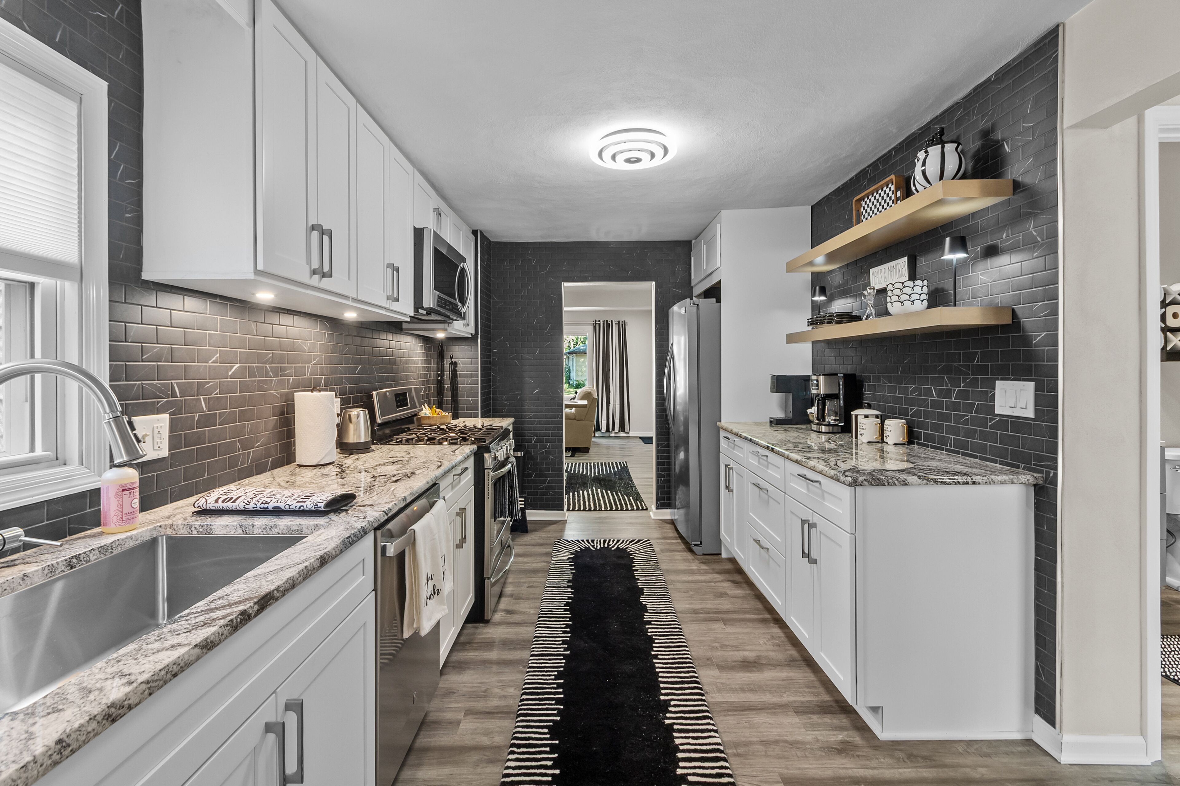 A modern kitchen with white cabinets, a black and white patterned rug, and a checkered shelf.