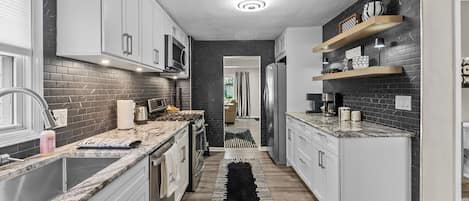 A modern kitchen with white cabinets, a black and white patterned rug, and a checkered shelf.