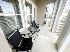 Ein Balkon mit zwei Stühlen und einem Tisch, großen Fenstern und Blick auf die Stadt.