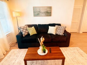 Ein Wohnzimmer mit einem dunkelgrauen Sofa, einem weißen Couchtisch und einem Gemälde an der Wand.