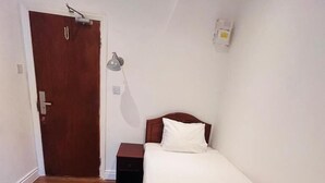 Et enkeltværelse med trægulv, et sengebord, en lampe og en dør.