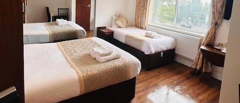 Habitación de hotel con dos camas, un espejo grande, una ventana con cortinas y suelo de madera.