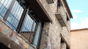 Un edificio de piedra con balcón, barandilla metálica y ventana con vistas.