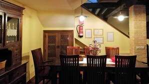 Un comedor con una mesa y sillas de madera, una araña y una escalera que sube a un nivel superior.