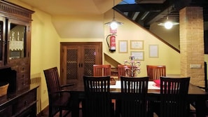 Un comedor con una mesa y sillas de madera, una araña y una escalera que sube a un nivel superior.