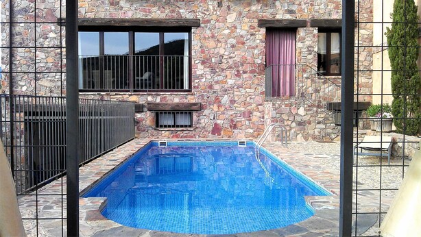 Un edificio de piedra con piscina, barandillas metálicas y un pequeño patio.