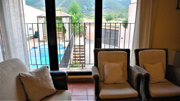 A balcony with wicker chairs and a view of a swimming pool and mountains.