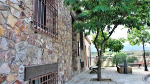 Edificio de piedra con banca de madera y un árbol en un patio.