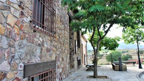 Edificio de piedra con banca de madera y un árbol en un patio.