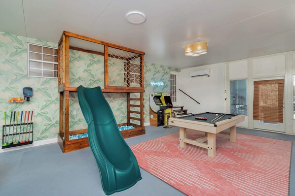 A room with a pool table, a slide, and a climbing structure.