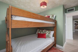 A bunk bed with a wooden frame, white bedding, and a red pillow.