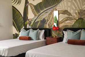 A hotel room with two beds, a nightstand, a lamp, and a large tropical-themed mural on the wall.