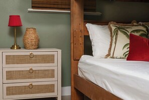 A bedroom with a wooden bed, white bedding, a red lamp, and a woven vase on a nightstand.