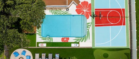 Eine Vogelperspektive auf ein Anwesen mit Swimmingpool, Tennisplatz und einer runden Lounge-Bereich mit Liegestühlen.