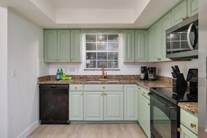 A kitchen with light green cabinets, a stainless steel microwave, a black dishwasher, and a granite countertop.