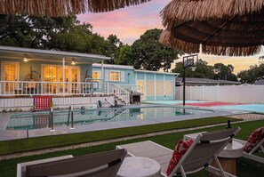 A swimming pool with a basketball hoop, lounge chairs, and a house with a porch.