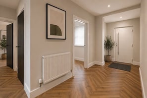 A hallway with wooden flooring, a radiator, and a framed picture on the wall. - Brand New • Bungalow • Driveway Parking • Office (Bedford)