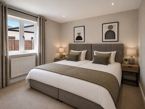 A bedroom with a large bed, two bedside tables, a window with curtains, and two wall-mounted artworks. - Brand New • Bungalow • Driveway Parking • Office (Bedford)