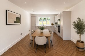 A modern kitchen with white cabinets, a wooden dining table, and a potted plant. - Brand New • Bungalow • Driveway Parking • Office (Bedford)