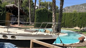A boat docked by a swimming pool with a thatched-roof structure nearby. - Casa del Mar Iznájar by Ruralidays (Córdoba)