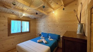 A wooden cabin room with a bed, a window with curtains, and a wooden cabinet. - Casa del Mar Iznájar by Ruralidays (Córdoba)