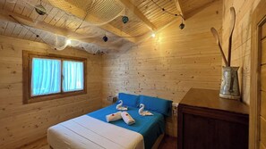 A wooden cabin room with a bed, a window with curtains, and a wooden cabinet. - Casa del Mar Iznájar by Ruralidays (Córdoba)