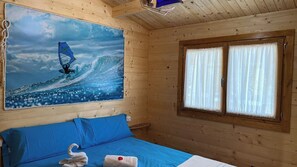 Une chambre avec un lit, une fenêtre avec des rideaux et un tableau représentant un surfeur.